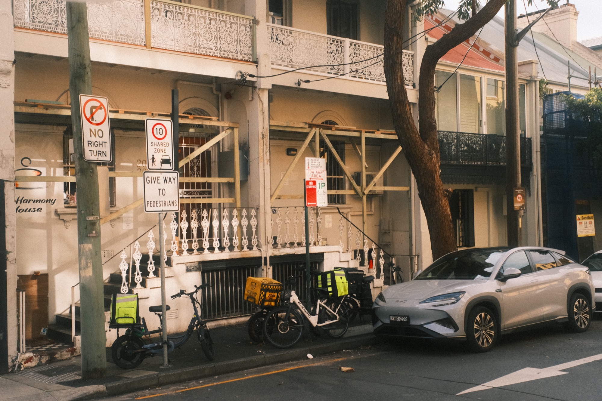 Scaffolding wraps the front of a terrace; two delivery bikes stand below it, one with a bag on the back. Nobody is with them.